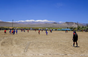 Soccer game at El Piñon - Match de foot à El Piñon Football game in San Pedro de Atacama, Argentina, with players on a dusty field and snow-capped moun.