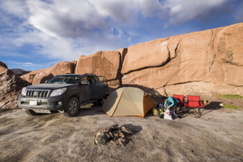 Bivouac - Salar de Talar Camping setup with tent and vehicle near large rock formations in Atacama Desert.