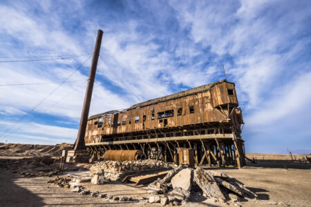 Oficina Santa Laura (UNESCO) Abandoned rusted train wreck in Fiambala, Argentina, under a vibrant blue sky with scattered clouds.