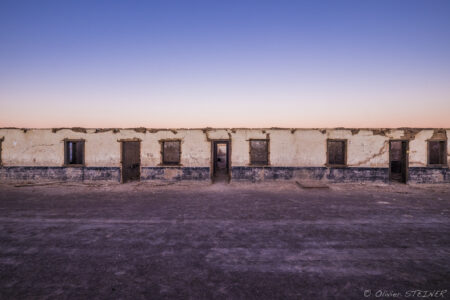 A rustic village scene in Fiambala, Argentina, captured at sunset, showcasing traditional adobe buildings and a tranquil desert atmosphere. Deserted village in Fiambala, Argentina, during sunset with colorful sky.