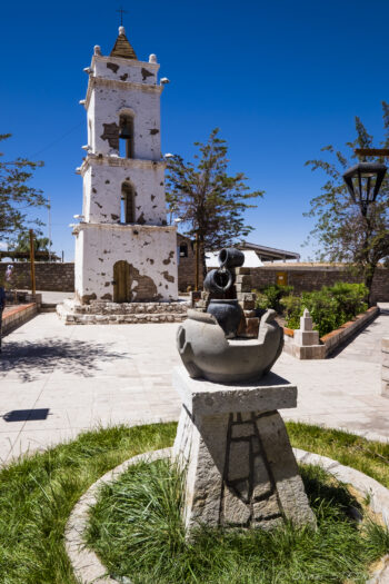 Toconao Historic church tower in San Pedro de Atacama with sculpture, clear blue sky, and surrounding greene.