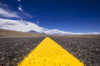 Back on the road - A nouveau sur la route Road in the Atacama Desert with a yellow line and mountains in the background.