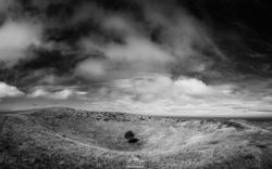 A black and white photograph capturing a peaceful landscape with rolling hills and a striking sky, emphasizing natural beauty and atmospheric mood. Black and white landscape photo of rolling hills and dramatic sky.