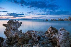 Tranquil lake scene during sunset featuring a rocky shoreline, calm waters, and a colorful sky reflecting on the surface. Beautiful lake at sunset with calm waters and rocky shoreline in the foreground.