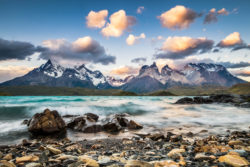 Spectacular sunset on the Cuernos de Paine, in Torres del Paine National Park, from Lake Pehoe Mountain landscape with rocky shoreline and dramatic sky at sunset.