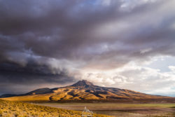 Stunning mountain landscape captured by Olivier Steiner Photography, showcasing dramatic weather and natural beauty. Mountain landscape with dark storm clouds and golden sunlight illuminating the terrain.