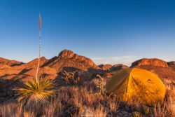 Camping in the desert mountains during sunset with a yellow tent and rugged terrain. Desert mountain landscape with a yellow tent and desert plants at sunset.