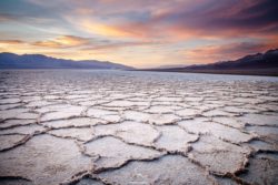 Stunning salt flats landscape during sunset with vibrant sky and textured ground, showcasing natural beauty and unique geological features. Salt flats with cracked surface under colorful sunset sky.