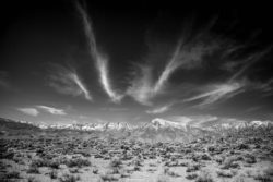 Stunning black and white photograph of a desert with mountains and dynamic cloud formations. Desert mountain landscape with snow-capped peaks and dramatic sky in black and white.