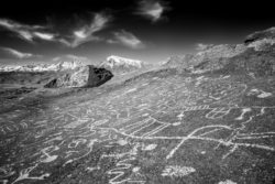 An impressive view of ancient geoglyphs etched into the hillside with mountains in the background. Black and white photo of ancient geoglyphs on a hillside in the Andes.