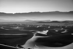 A stunning black and white photograph of vast sand dunes in a desert, highlighting textures and shadows for a captivating visual. Desert landscape with rolling sand dunes under a cloudy sky, captured in black and white for a drama.