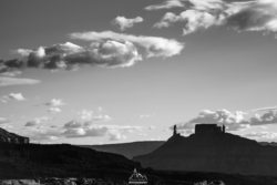 Black and white mountain landscape featuring dramatic clouds and a distant castle silhouette. Sunset over rugged mountain landscape with dramatic clouds in black and white.
