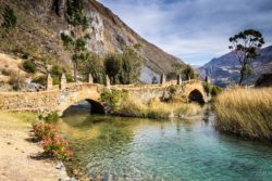 Serene mountain river scene with a stone bridge, surrounded by trees and mountains in the background. Beautiful mountain river with clear water and lush greenery.