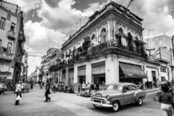 A black and white photograph capturing a lively Havana street with vintage cars, pedestrians, and historic buildings. Vintage Havana street scene with classic cars and colonial architecture.