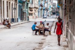 Cuban street life captured with locals enjoying a game of dominoes on a sunny day in Havana. Vibrant street scene in Havana with locals playing dominoes and walking along colorful historic buil.
